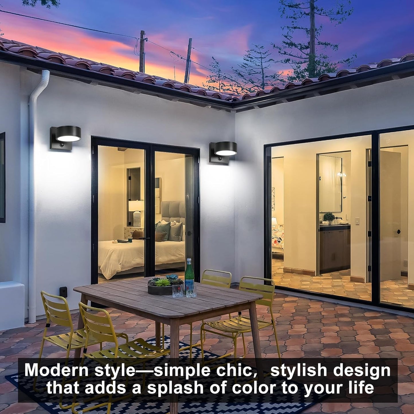 Modern outdoor patio with glass doors leading to a bedroom and bathroom, featuring a wooden table and chairs.